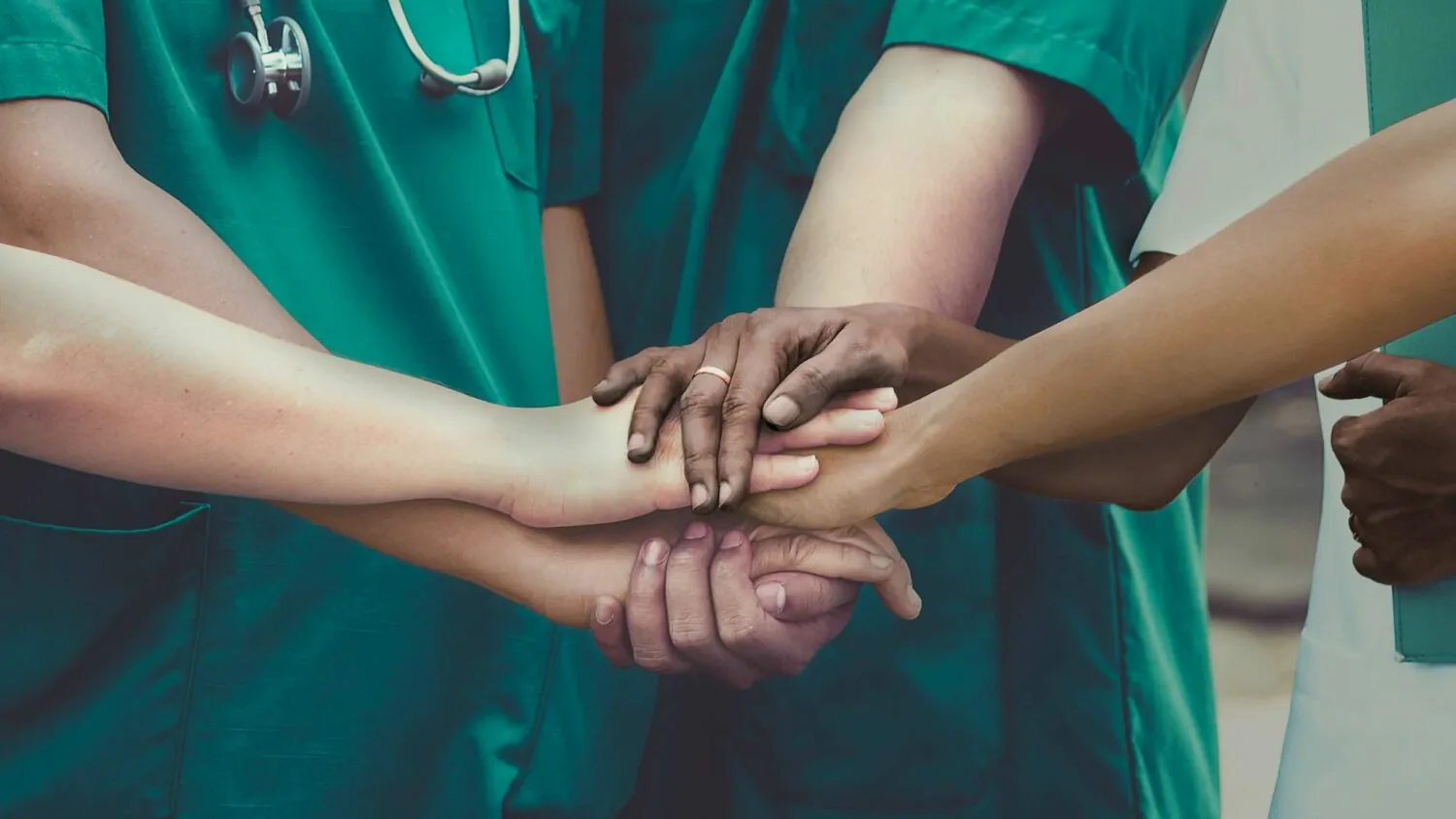 Group of doctors in green scrubs holding the top of each others hands.