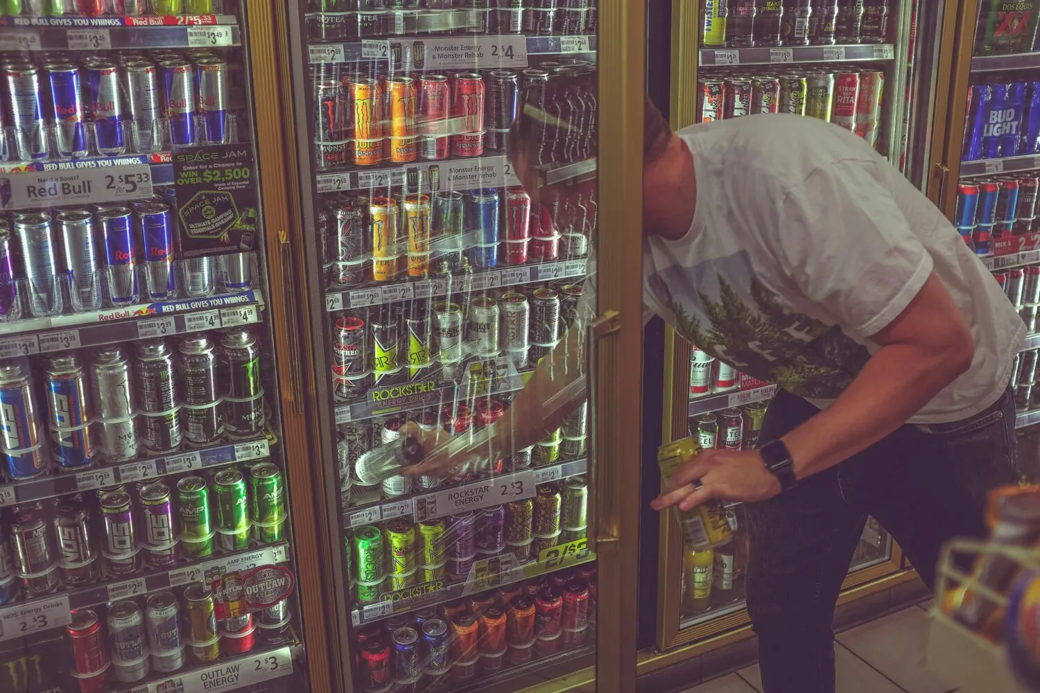 A man taking a high-caffeine energy drink out of a chiller cabinet.