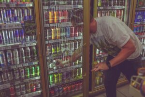 A man taking a high-caffeine energy drink out of a chiller cabinet.